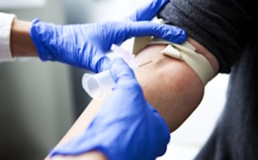 Close up of blood been drawn by a health worker wearing blue gloves on the inner elbow of a patient